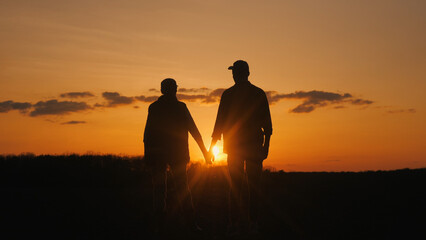 Couple holding hands as the sun sets over the grassy field