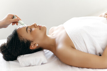 Side view of well-groomed hispanic or brazilian woman, wrapped in a towel, lying during a skincare...