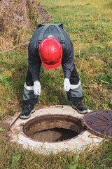 A worker looks into a septic sewer well, checking for water accumulation. Plumbing work