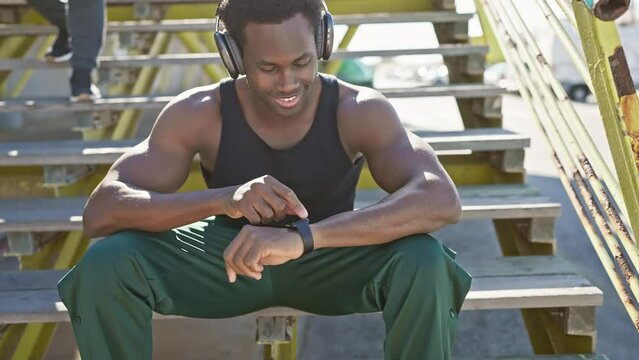 African american man listening to music with headphones and checking smartwatch on city bleachers outdoors