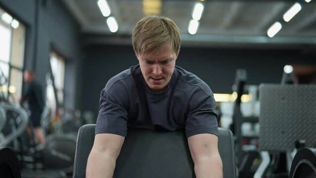 Portrait of motivated beginner sportsman hard time doing Scott Curls with barbell sitting on preacher curl bench and lifting up EZ-bar. Concept of healthy lifestyle, physical sport activity.
