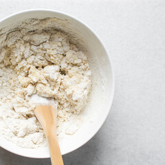 Overhead view of coco bread dough being mixed in a white bowl, jamaican bread dough on a marble countertop, process of making coco bread