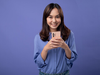 Excited Asian woman celebrating good news on her smartphone, wearing a stylish blue blouse and...