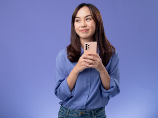 Excited Asian woman celebrating good news on her smartphone, wearing a stylish blue blouse and...
