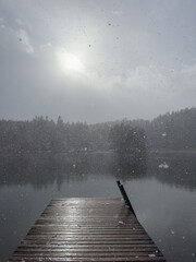 A solitary wooden pier on a snowy lake under a hazy sun, evoking a quiet winter's day.