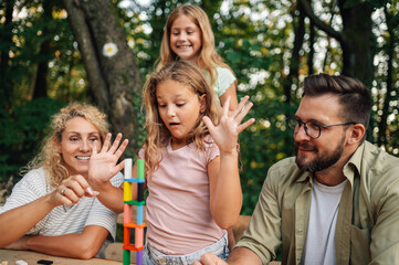 Cheerful family playing fun board game at picnic table in nature.