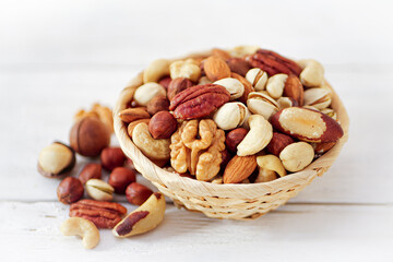 Nuts Mix in a Wooden Plate on a White Background. Wicker Basket full of Cashew, Walnuts, Hazeltuts, Peanuts, Brazilian Nuts, Pistachios