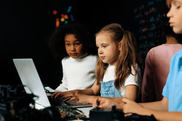 Smart girl in white bib learning about coding robotics technology using laptop in the STEM class....