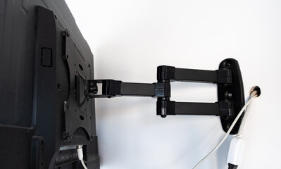 Flat screen TV hanging on a metal mount on the white wall in the room. Black TV bracket, mount...
