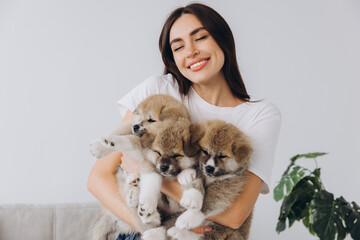 Happy smiling millennial woman owner of Akita Inu puppies playing with dogs at home holding and hugging them, space for text or copy