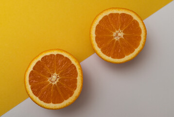 Two oranges are cut in half and placed on a yellow and white background. The oranges are ripe and juicy, and their bright orange color contrasts with the neutral background