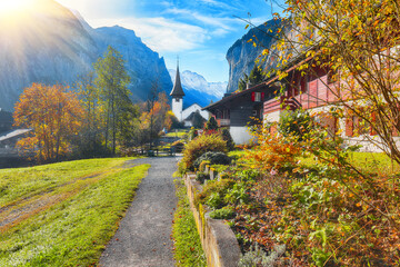 Amazing autumn landscape of touristic alpine village Lauterbrunnen with famous church and Staubbach waterfall.