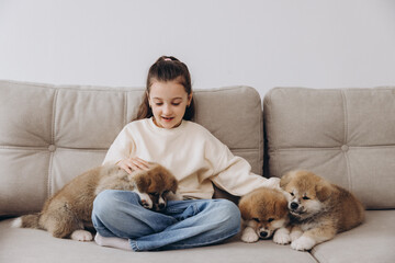 Little happy smiling girl playing and hugging Akita Inu puppies at home on sofa