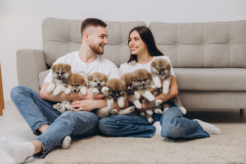 Beautiful smiling happy couple playing with akita inu puppies in dog house or shelter