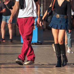 young man and girl, millennial couple walking down a busy street, their lower half in focus. Red trousers and a denim skirt with high black boots are the look of urban life and fashion