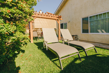  Backyard with two lounge chairs beside a pergola on a sunny day. - 794441224