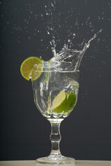 Lemon falling into a glass of transparent water causing splashes upwards. Isolated on gray background.