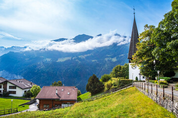 Wengen town in Switzerland. View over Swiss Alps near Lauterbrunnen valley. Church and houses in Wengen. Mountain peak covered with clouds on sunny day