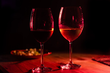 Photograph of two glass glasses of wine on a wooden table with salad in the background.