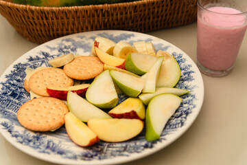 Breakfast plate with banana, apple, pear, biscuit, cheese and yogurt on a table.