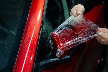 The master applies vinyl film to the side view mirror of a car. 