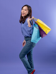 Joyful shopper with colorful bags, blue blouse, denim jeans, and red flats on a purple backdrop