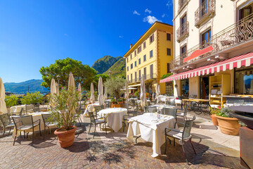 A lakefront sidewalk cafe on Piazza Garibaldi on a clear summer day in the picturesque Italian village of Menaggio, Italy, on the shores of Lake Como.