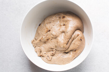 Overhead view of hot cross bun dough proofing in a white mixing bowl, bread dough resting in a...