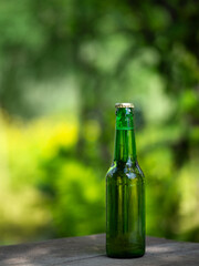 glass bottle of light beer on the table in the garden. Green background