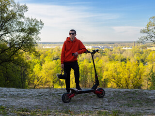 happy young man on an electric scooter, nature background. Helmet in hand