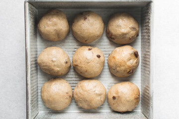 hot cross bun dough rising in a silver baking pan, bun dough rolled into balls in a baking tin,...