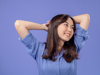 Naklejka premium Portrait of an Indonesian Asian woman, wearing a blue shirt, smiling with her hands behind her head, isolated against a purple background