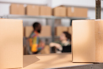 Selective focus of cardboard boxes in warehouse, in background diverse team preparing customers...