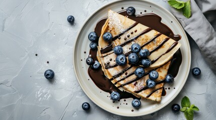 Crepes, thin pancakes with chocolate sauce and fresh blueberries. Grey background. Copy space. Top view.