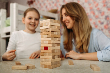 Mother and daughter playing a game with wooden blocks at home.