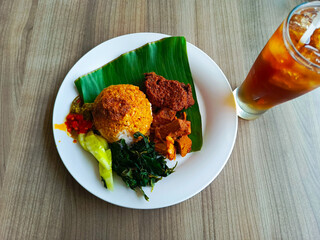 A plate of complete Nasi Rendang meal served with sweet iced tea, showcasing a flavorful Indonesian culinary experience in one serving