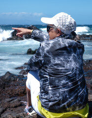 Rear view of Mature woman sitting on a rocky beach while admiring the sea waves and the power of...