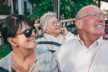 Smiling senior happy caucasian retired people sitting on sightseeing open-top bus visiting city of Cordoba listening audio guide, Andalusia, Spain.