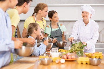 Team of teenagers and female chef at cooking classes. Learn to beat raw eggs