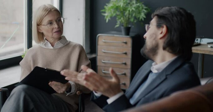 Professional female therapist talking to male client discussing psychological aid and treatment in office. Communication and therapy session concept.