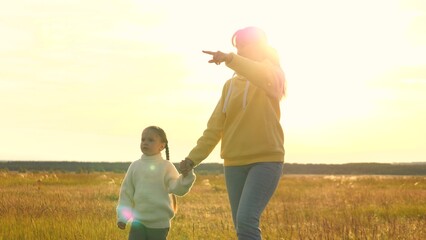 Woman holds girl hand. Child, kid and mother walk against background bright rays light shining sun....