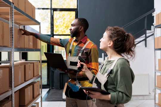 Diverse storehouse employees checking cardboard boxes, scanning products for inventory using store scanner in warehouse. Stockroom supervisors working at clients orders preparing packages for delivery