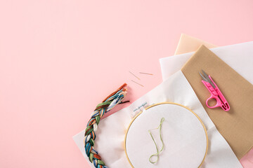 Flat lay composition with cross stitch embroidery and sewing accessories on pink background