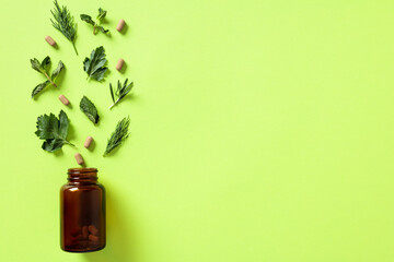 Amber glass bottle with natural herbal dietary supplements on green background. Flat lay, top view, copy space.