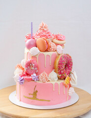 Pink layered tall cake with pink frosting, cake pops, macaroons, meringues, donuts and golden figure of gymnast girl