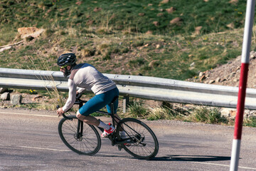 A man riding a bicycle on a road descending at high speed. There is a red and white pole