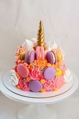 Unicorn cake with golden fondant horn, eyelashes and pink, orange, purple cream cheese frosting on neutral background