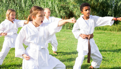Kids in kimono doing kata moves during outdoor karate training.