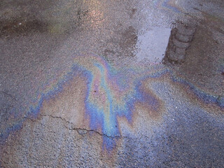 Gasoline fuel stains, gas spill spots or rainbow oil slicks on a wet city asphalt road. Urban...