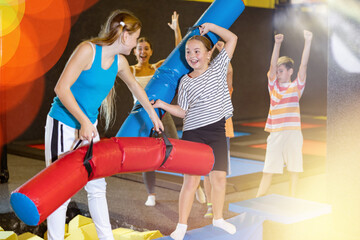 Active excited child school girls having fun and fighting with inflatable logs in amusement center